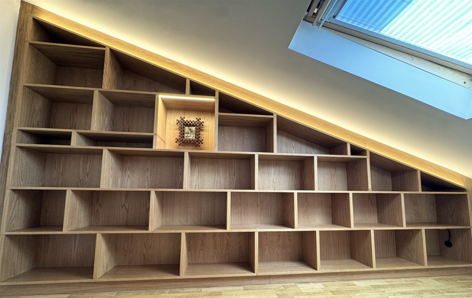 Wall-to-wall oak bookcase stepped to follow a sloping ceiling, with LED lighting along the slope